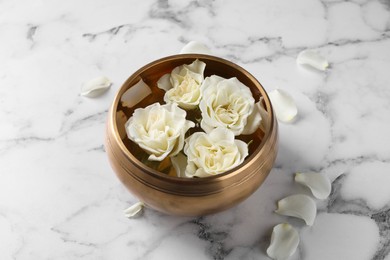 Photo of Tibetan singing bowl with water and beautiful roses on white marble table
