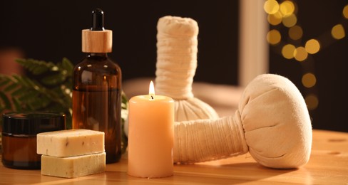 Photo of Spa composition. Cosmetic products, herbal bags and burning candle on wooden table, closeup