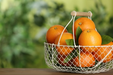 Photo of Fresh ripe oranges in basket on wooden table against blurred background. Space for text
