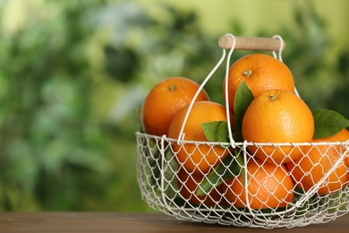 Fresh ripe oranges in basket on wooden table against blurred background. Space for text