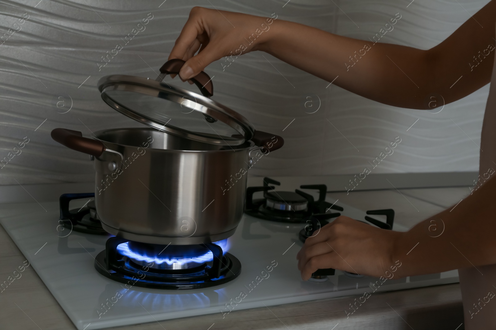 Photo of Woman near gas stove with pot in kitchen, closeup