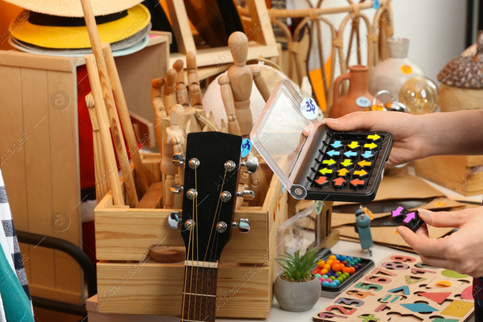 Photo of Woman holding smart game IQ near table with different stuff indoors, closeup. Garage sale