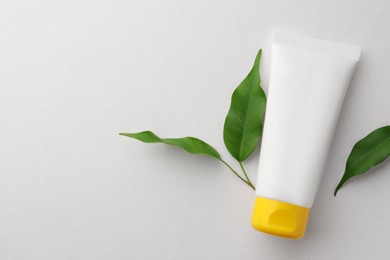 Photo of Tube of face cream and green leaves on white background, flat lay. Space for text