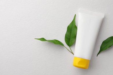 Tube of face cream and green leaves on white background, flat lay. Space for text