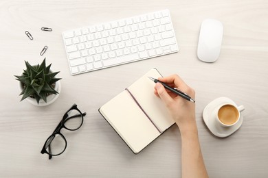 Woman writing in notebook at light wooden table, top view