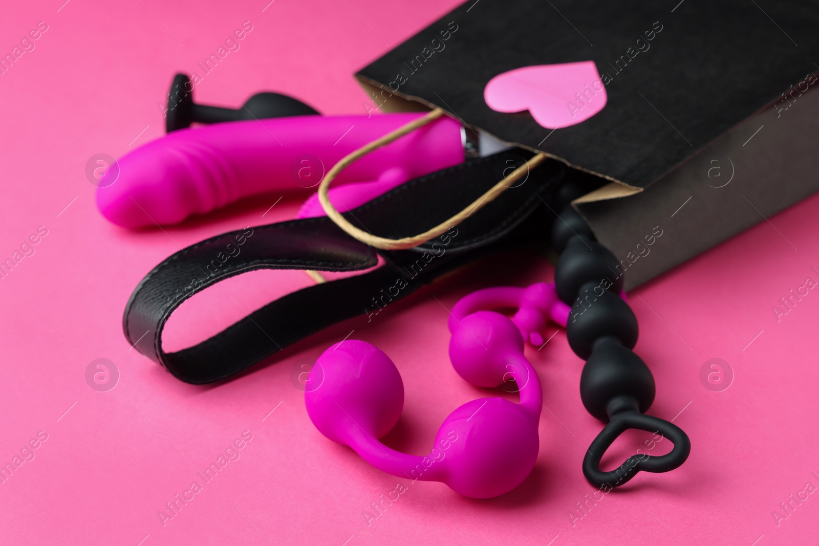 Photo of Shopping bag with different sex toys on pink background, closeup