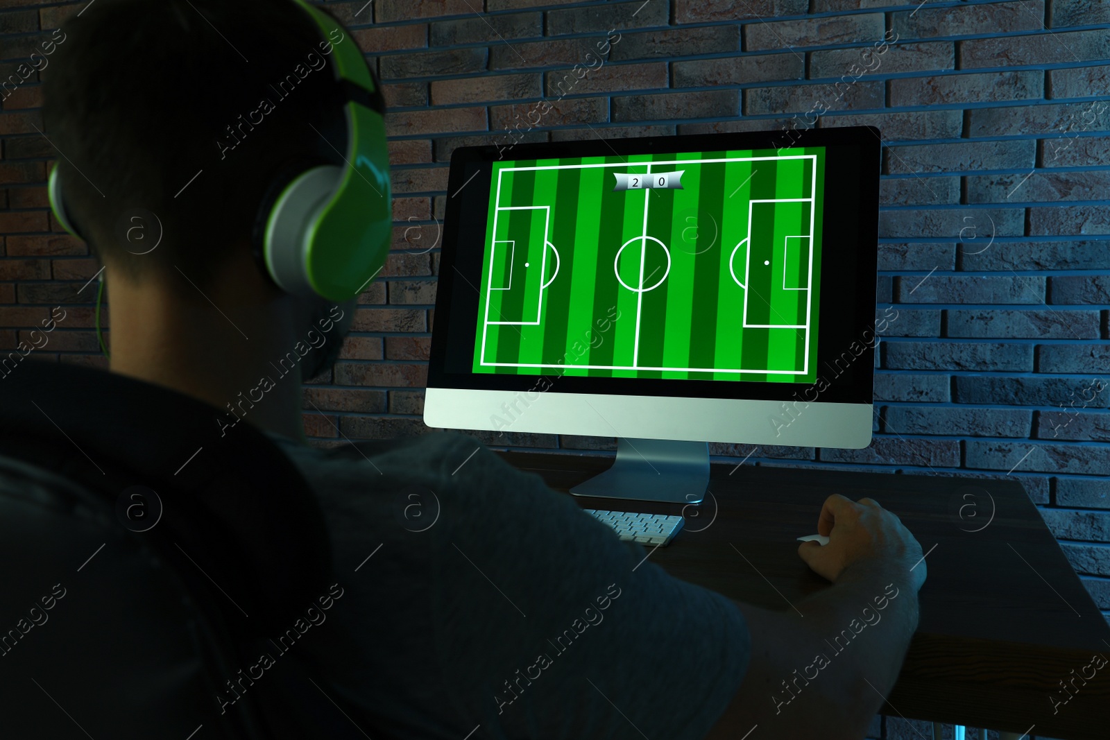 Photo of Man with headphones playing video game at table in dark room