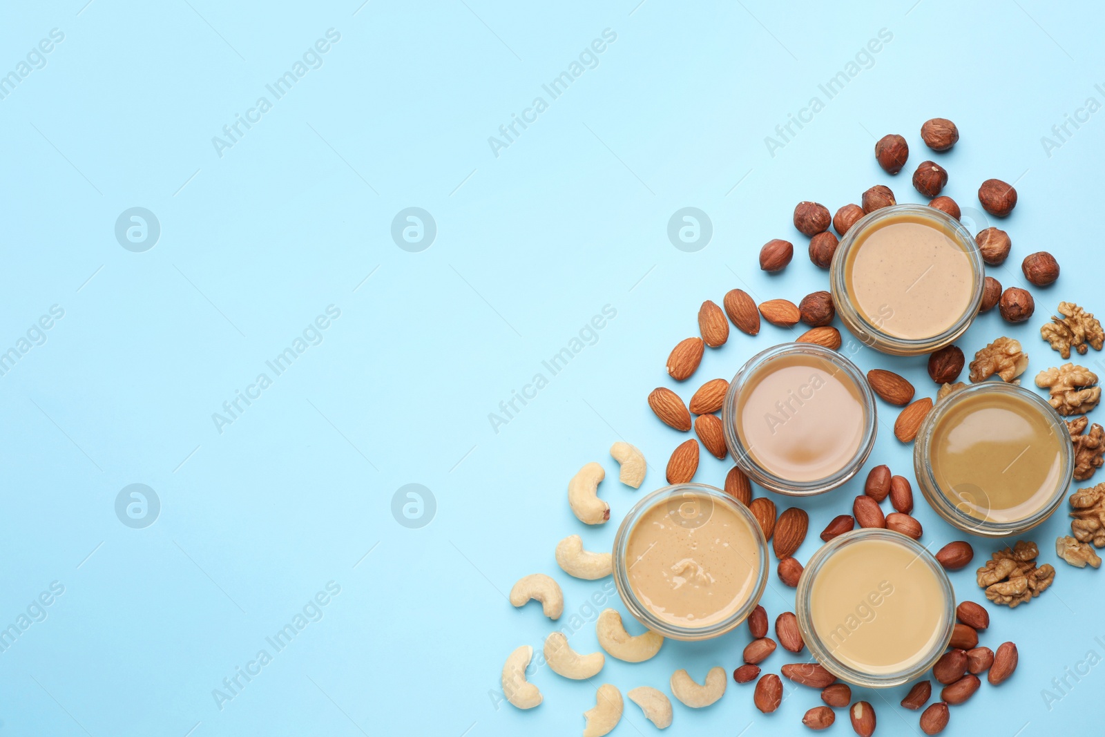 Photo of Different types of delicious nut butters and ingredients on light blue background, flat lay. Space for text