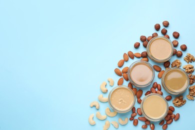 Different types of delicious nut butters and ingredients on light blue background, flat lay. Space for text