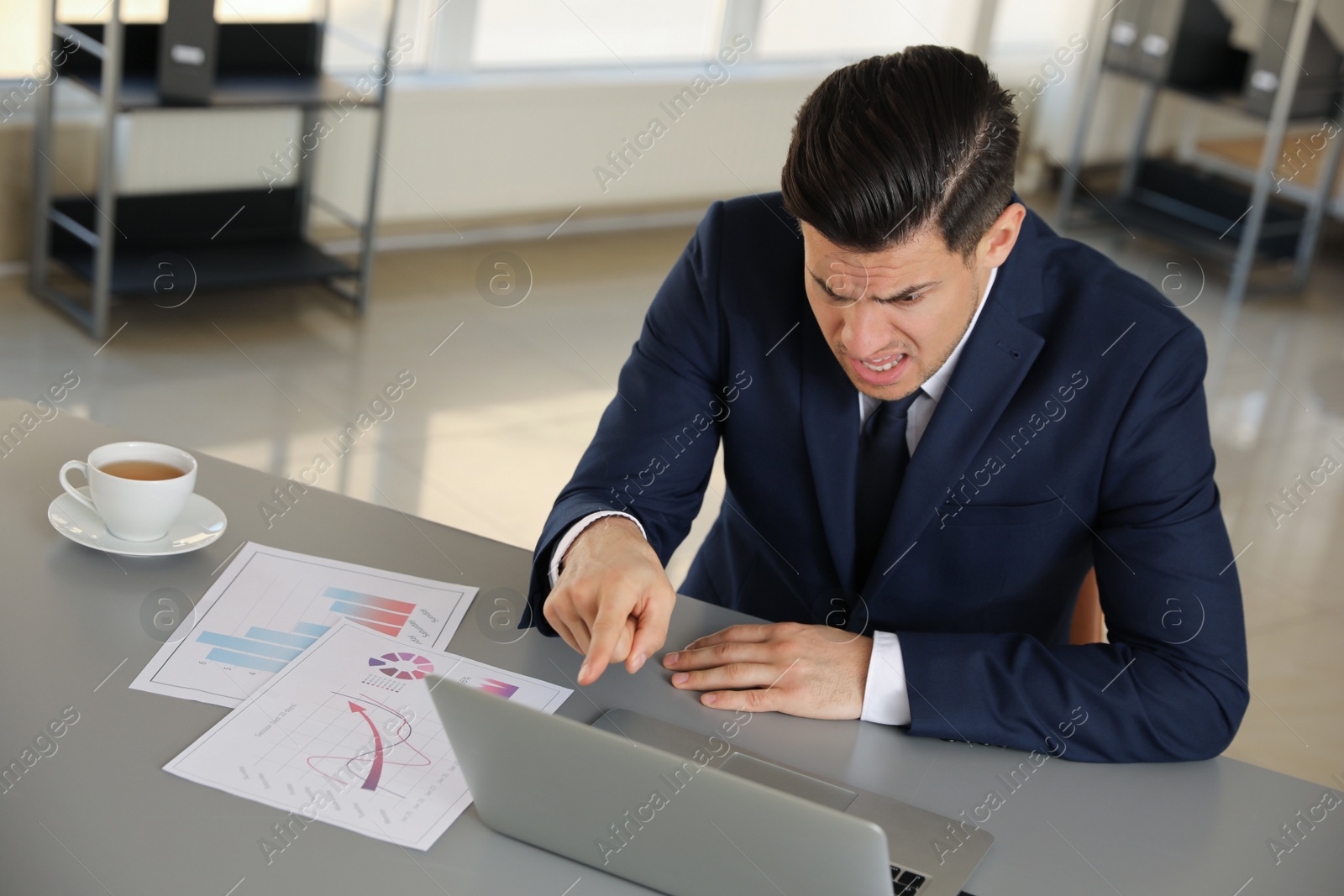 Photo of Emotional businessman with laptop at table in office