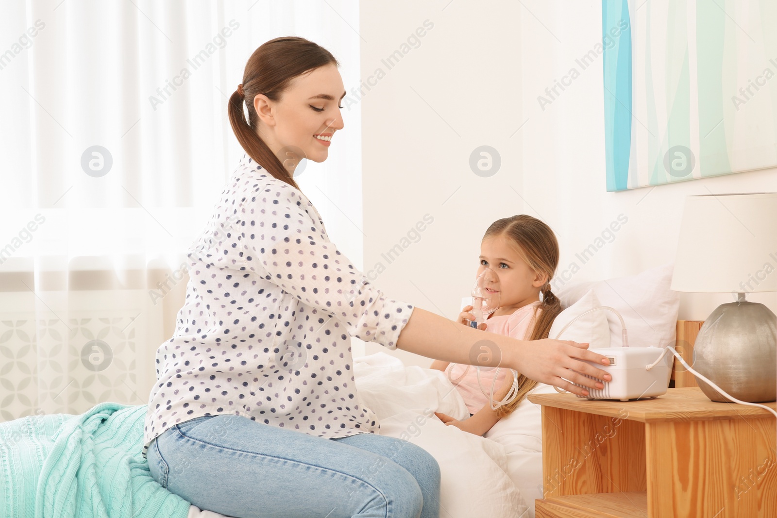 Photo of Mother helping her sick daughter with nebulizer inhalation in bedroom