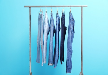 Photo of Rack with stylish jeans on color background