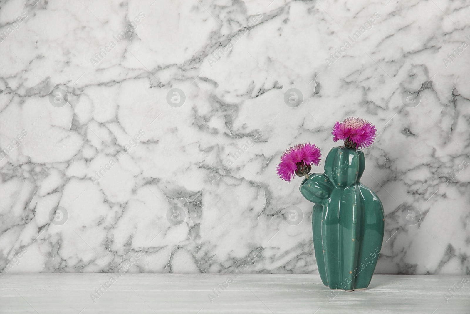 Photo of Trendy cactus shaped ceramic vase with flowers on table against marble background