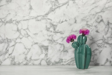 Trendy cactus shaped ceramic vase with flowers on table against marble background