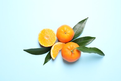 Flat lay composition with fresh ripe tangerines and leaves on light blue background. Citrus fruit