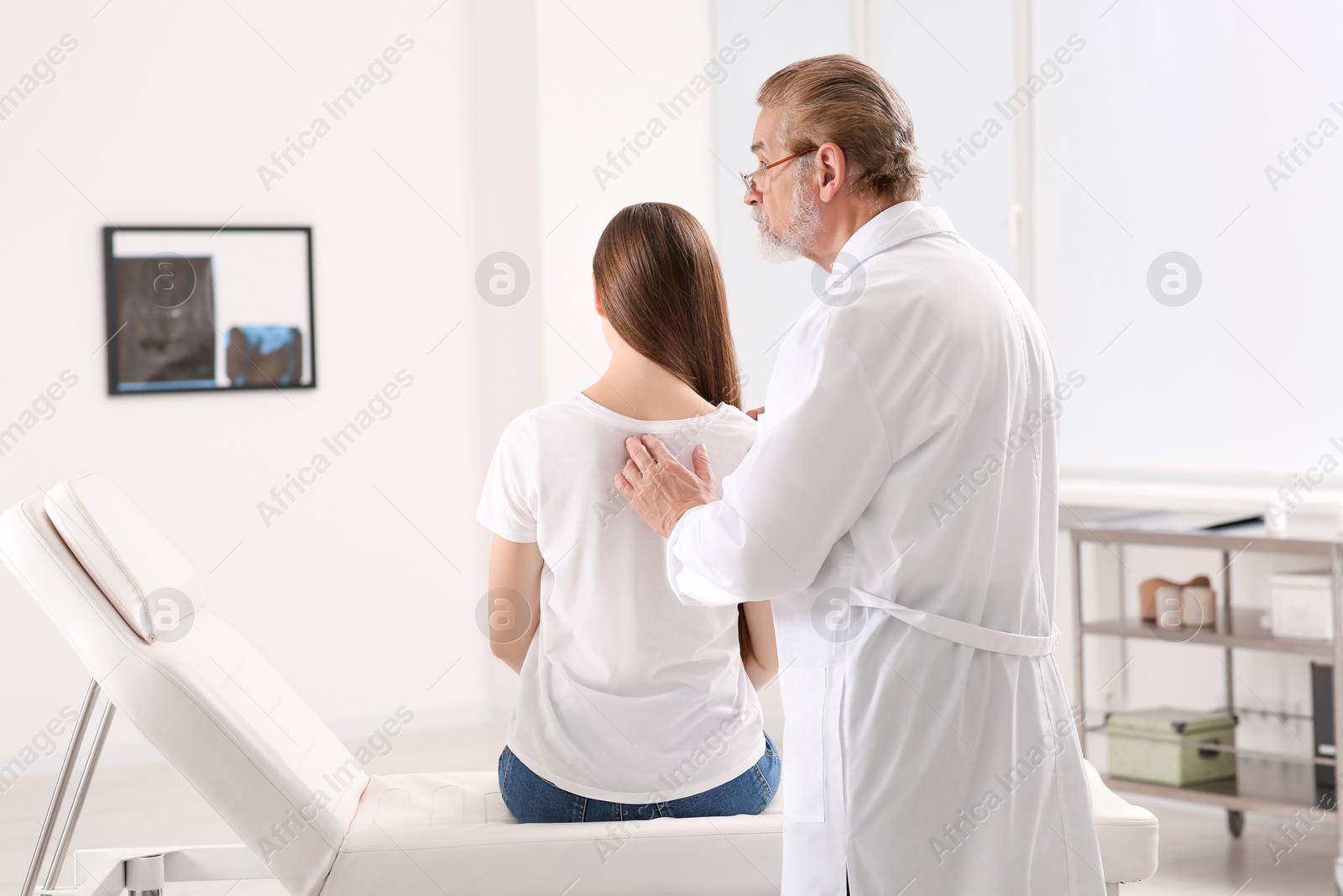 Photo of Professional orthopedist examining patient's back in clinic