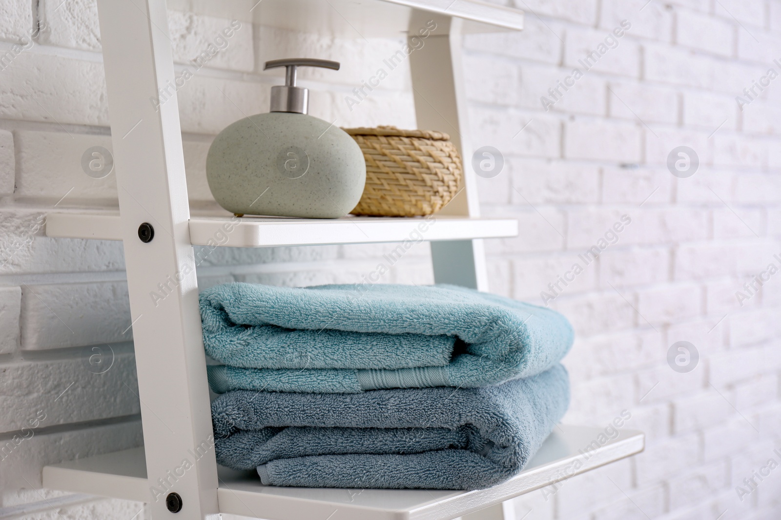 Photo of Clean soft towels and soap dispenser on shelves near white brick wall