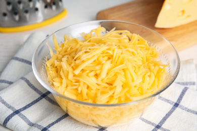 Photo of Delicious grated cheese in glass bowl on table, closeup