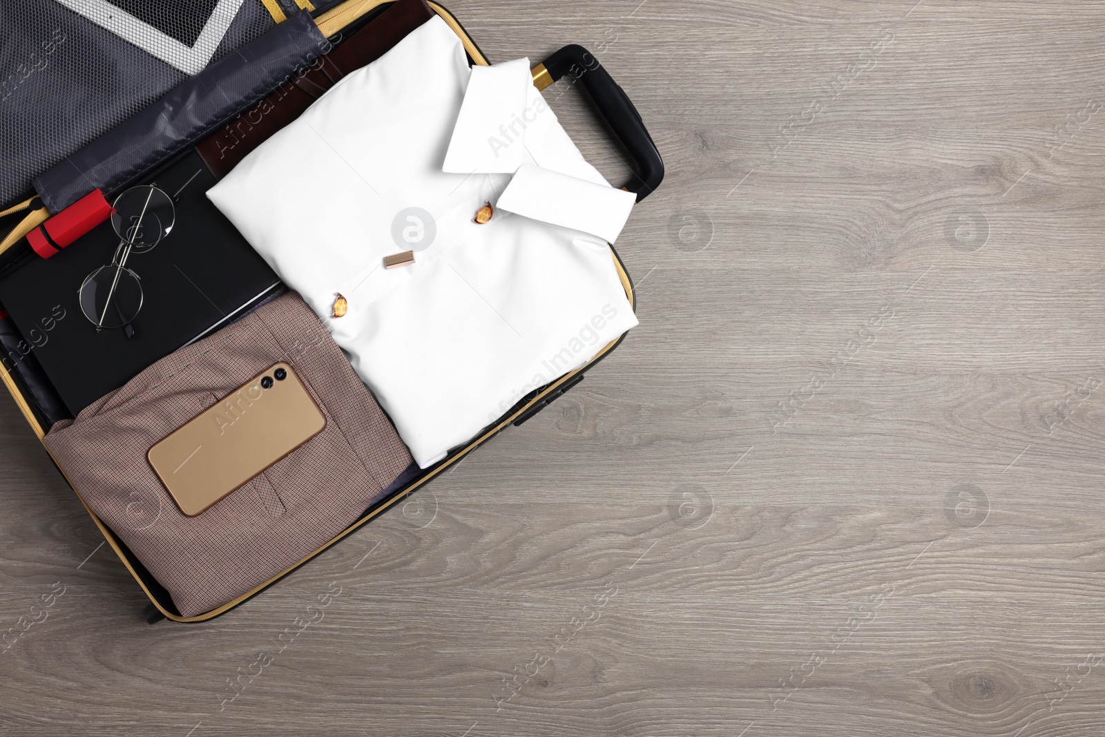 Photo of Folded clothes and accessories in open suitcase on wooden background, top view with space for text. Business trip preparations