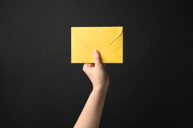 Photo of Woman holding yellow paper envelope on black background, closeup