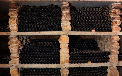 Photo of Many wine bottles on shelves in cellar