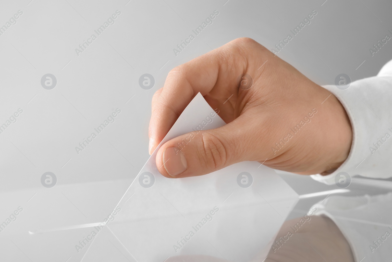 Photo of Man putting his vote into ballot box on light background, closeup