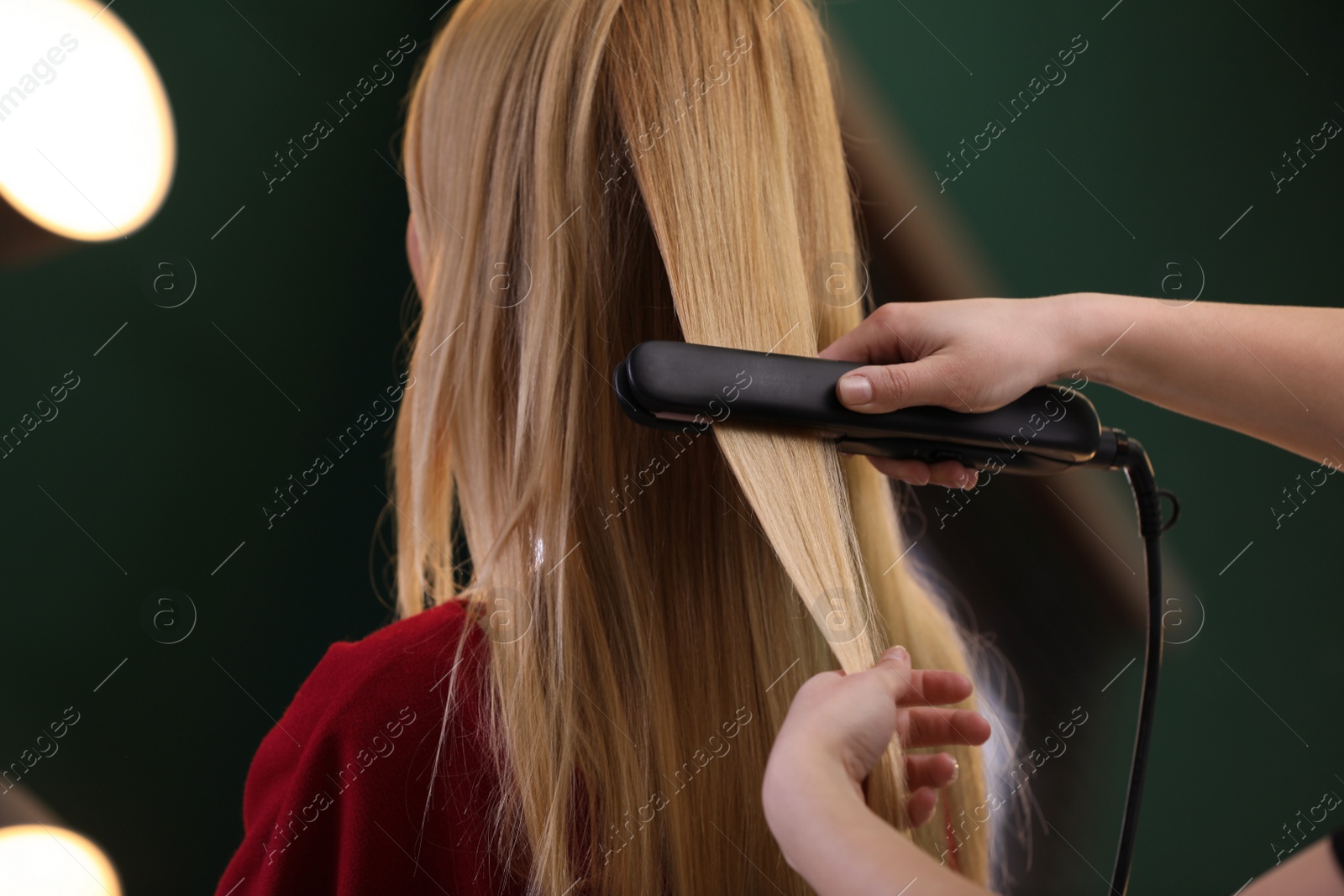 Photo of Stylist straightening woman's hair with flat iron in salon