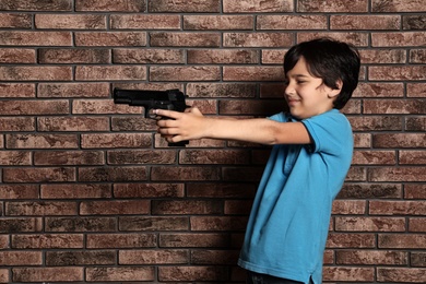 Photo of Little child playing with gun against brick wall. Dangerous game