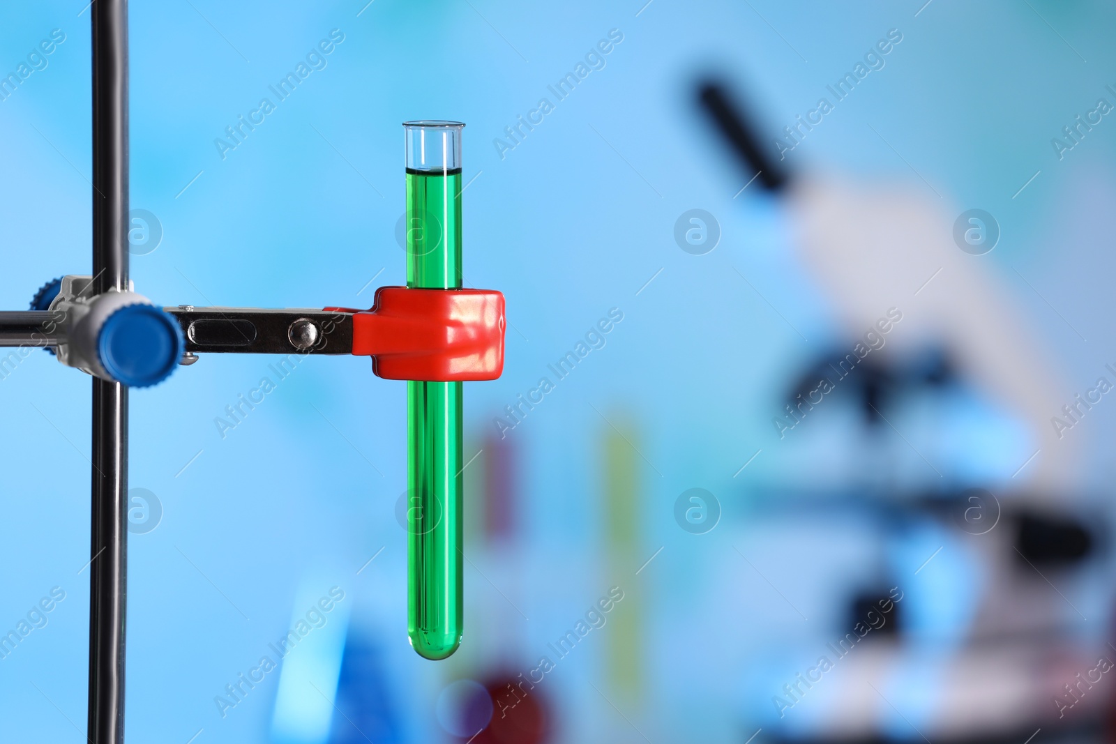 Photo of Test tube with green liquid on retort stand in laboratory, closeup. Space for text