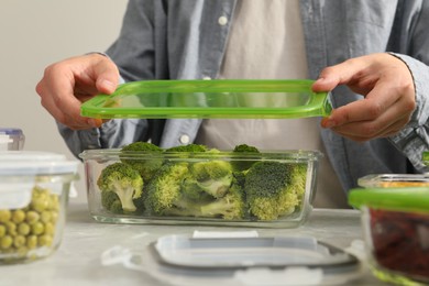 Photo of Man closing glass container with lid at light grey marble table in kitchen, closeup. Food storage