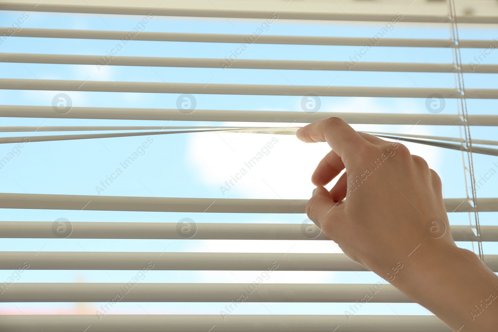 Photo of Woman opening horizontal window blinds at home, closeup. Space for text