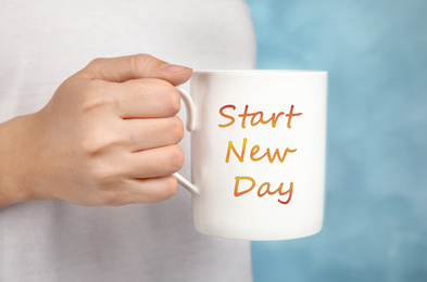 Image of Woman holding cup with phrase START NEW DAY on light blue background, closeup