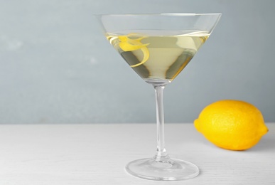 Glass of lemon drop martini cocktail with zest on white wooden table against grey background. Space for text