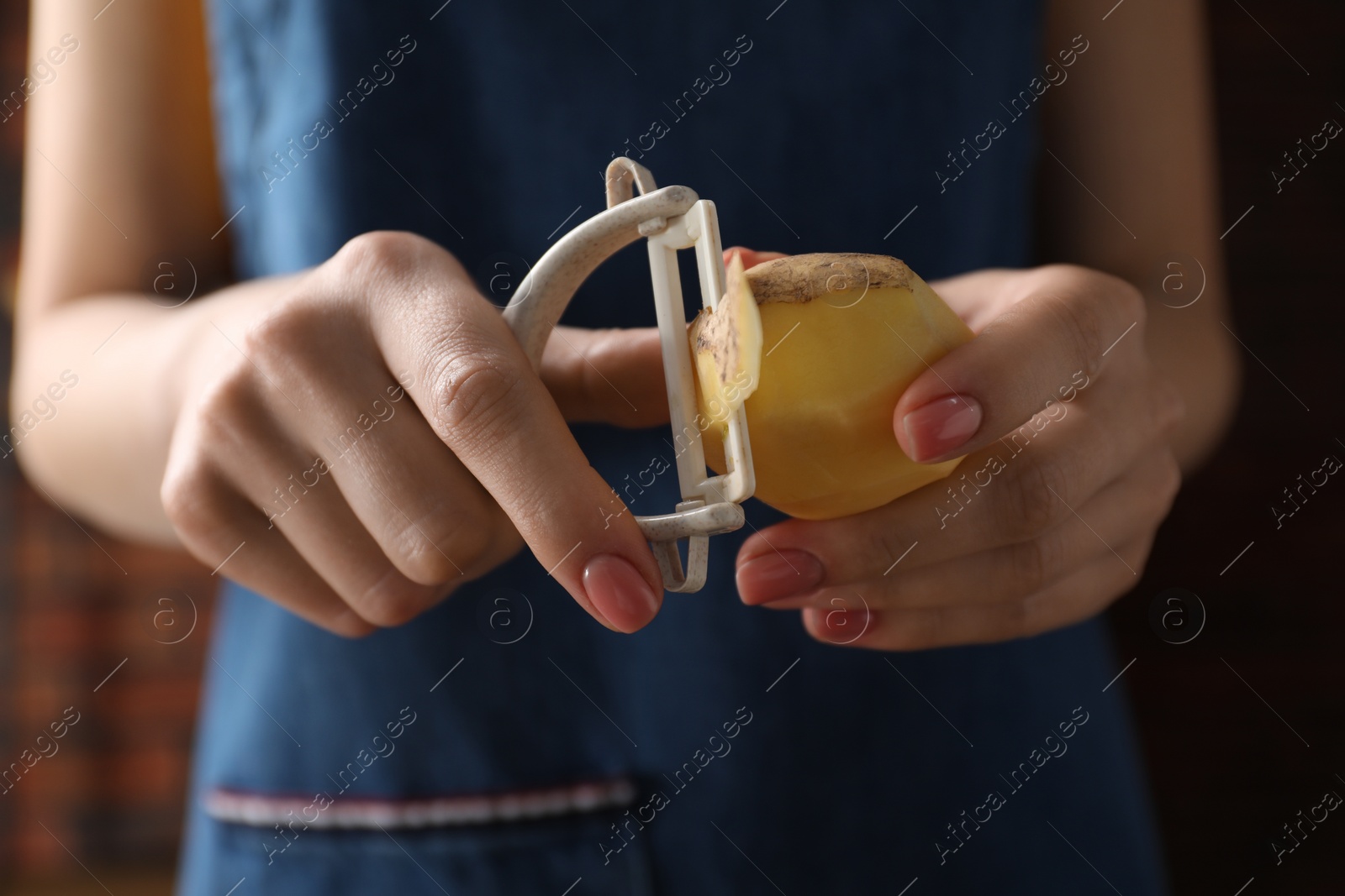 Photo of Woman peeling fresh potato indoors, closeup view