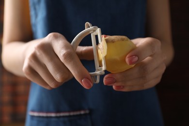 Photo of Woman peeling fresh potato indoors, closeup view