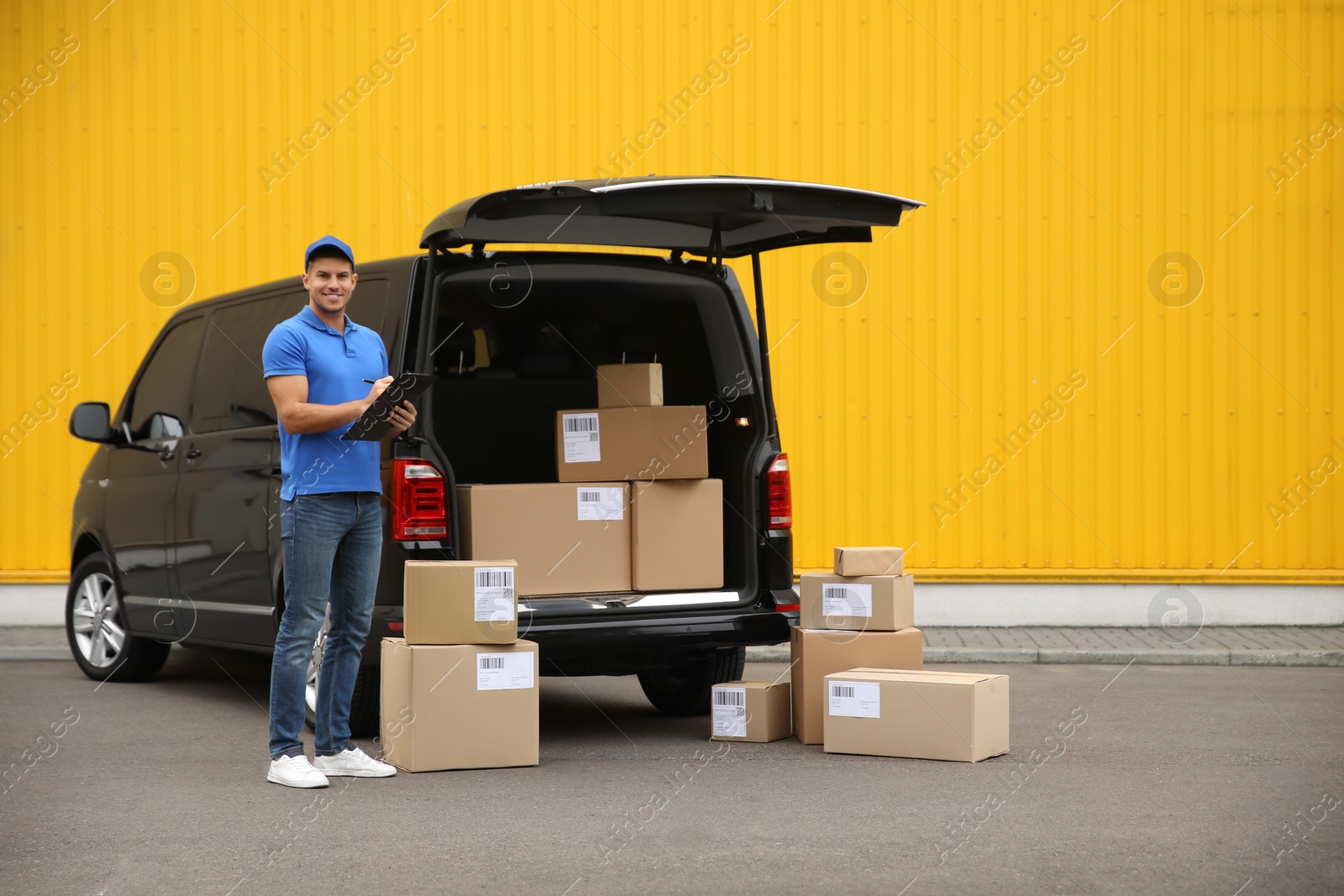 Photo of Courier with clipboard and parcels near delivery van outdoors