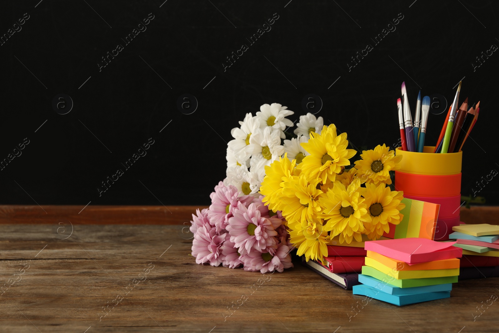 Photo of Set of stationery and flowers on wooden table near chalkboard, space for text. Teacher's Day