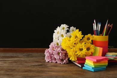 Set of stationery and flowers on wooden table near chalkboard, space for text. Teacher's Day