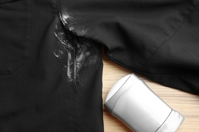 Photo of Black shirt with stain and deodorant on wooden background, closeup