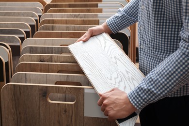 Photo of Man with sample of light wooden flooring in shop, closeup