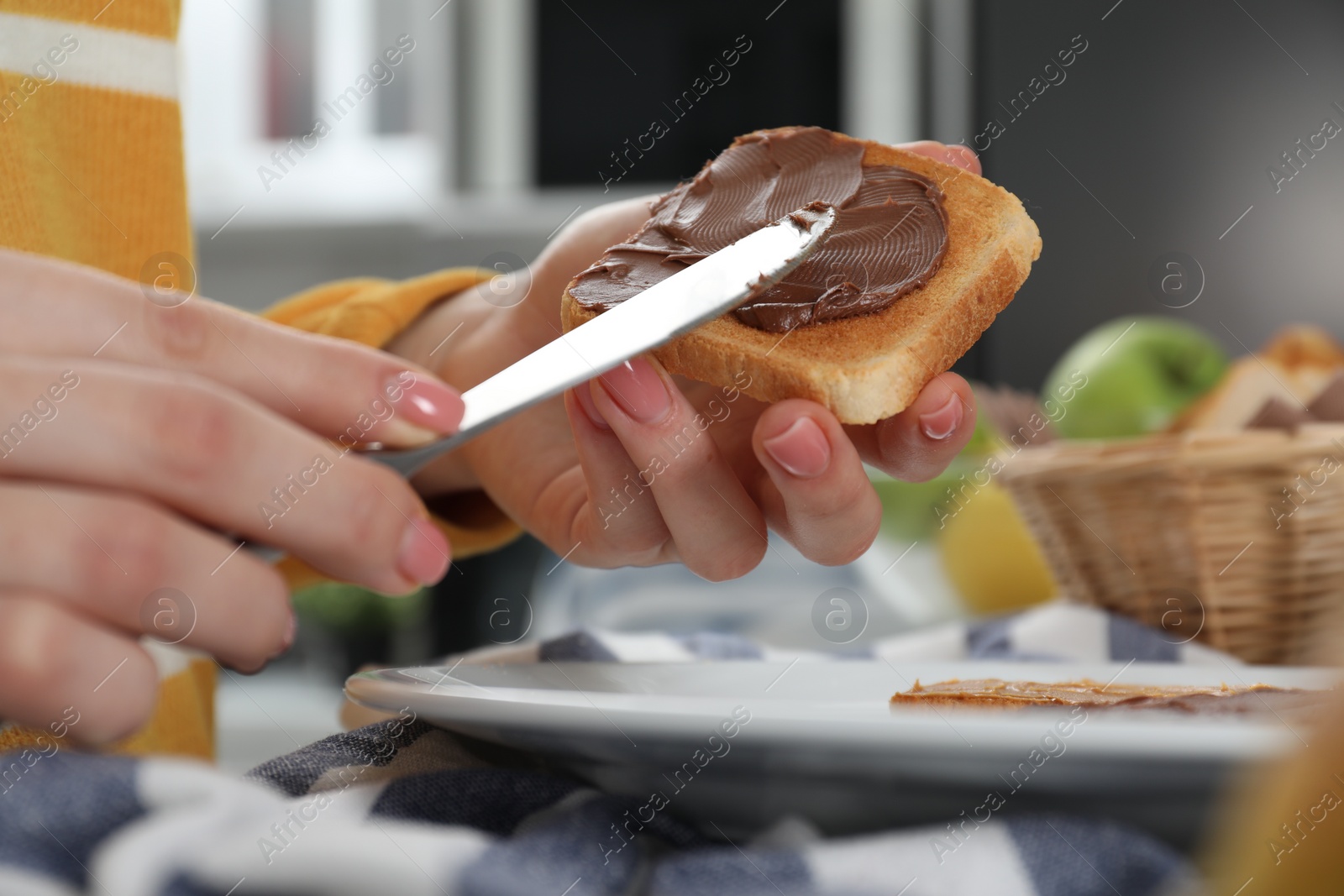 Photo of Woman spreading tasty nut butter onto toast indoors, closeup