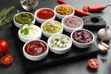 Photo of Different tasty sauces in bowls and ingredients on grey table