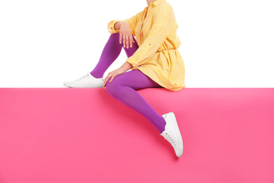 Woman wearing bright tights and stylish shoes sitting on color background, closeup