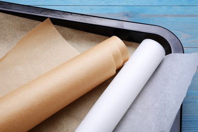 Photo of Rolls of parchment paper in baking pan on light blue wooden table, closeup