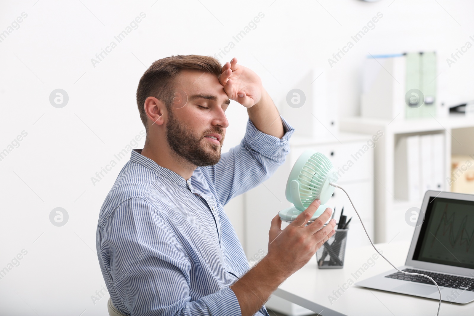 Photo of Man enjoying air flow from fan at workplace