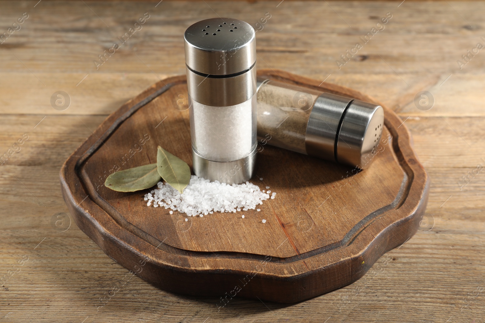 Photo of Salt and pepper shakers with bay leaves on wooden table