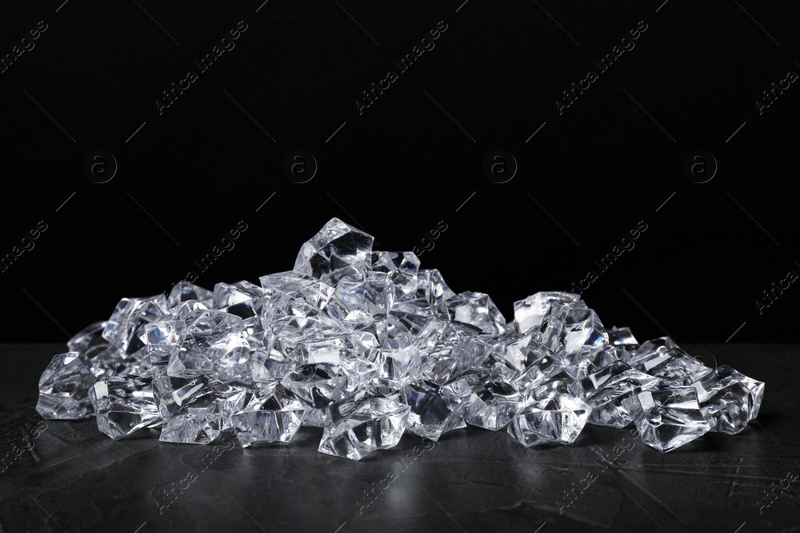 Photo of Pile of crushed ice on grey table against black background