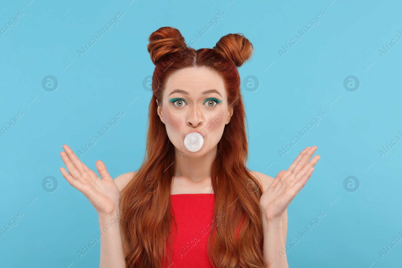 Photo of Portrait of surprised woman with bright makeup blowing bubble gum on light blue background