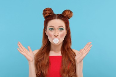 Photo of Portraitsurprised woman with bright makeup blowing bubble gum on light blue background