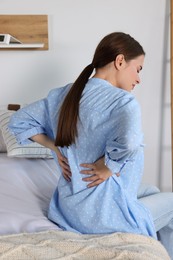 Photo of Woman suffering from back pain while sitting on bed at home. Symptom of scoliosis